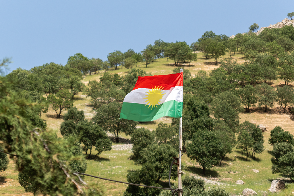 de Koerdische vlag wappert in de wind boven een heuvelachtig landschap met eikenbomen in het noorden van Irak