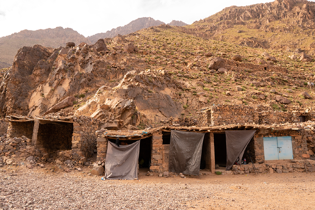Stenen hutten met canvas luifels staan aan de voet van een ruige, droge bergwand in een afgelegen gebied.