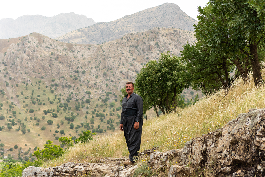 Koerdische man in traditioneel gewaad poseert trots op een bergpad in het ruige, groene landschap van Iraaks Koerdistan
