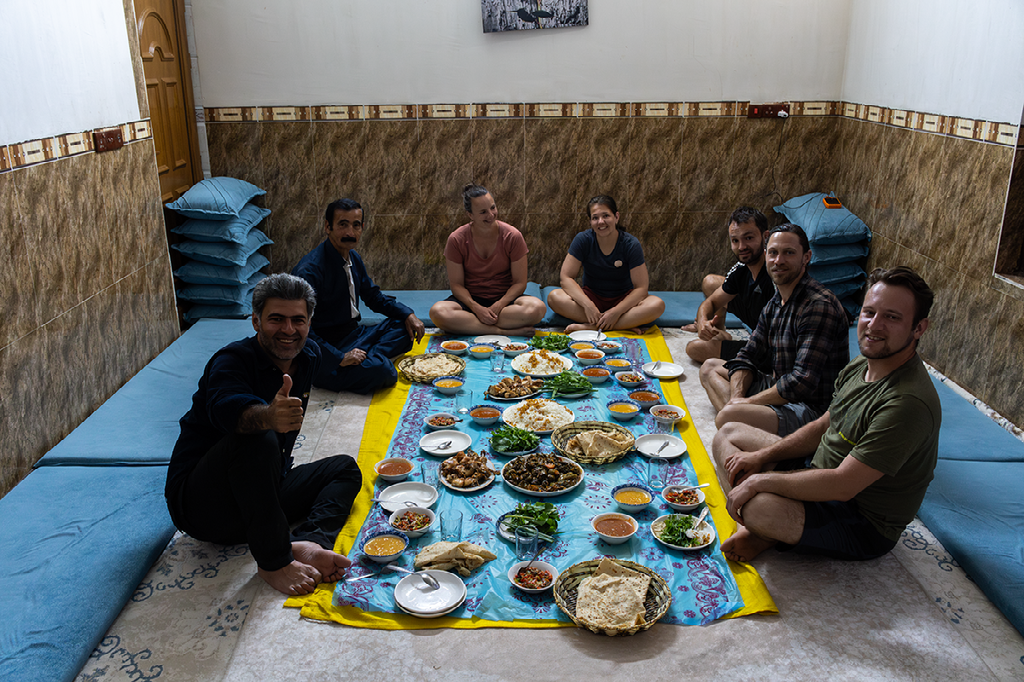 Reizigers en Koerden delen samen een traditionele huisgemaakte maaltijd op de vloer, omringd door warme gastvrijheid en lokale gerechten