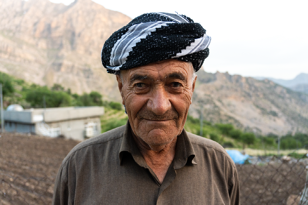 portret van een oudere man met traditionele hoofddoek voor een bergachtig landschap