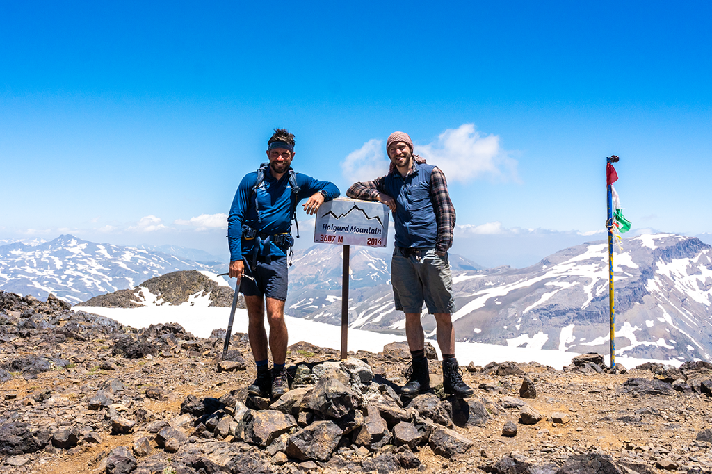 Twee bergwandelaars poseren op de besneeuwde top van de Halgurd Mountain in Koerdistan, met op de achtergrond een spectaculair uitzicht over ruige bergkammen en een Koerdische vlag die wappert in de wind