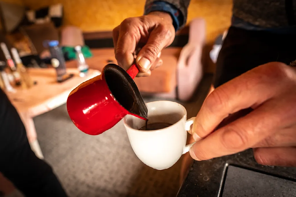 Close-up van handen die koffie uit een rode cezve in een witte kop schenken.