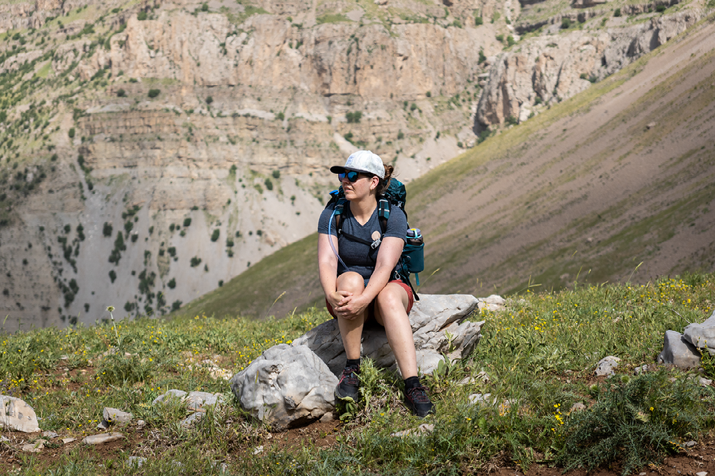 vrouw met rugzak rust uit op een steen tussen het berggras in een zonnige vallei omringd door steile rotswanden