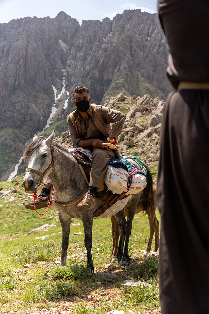 man op een ezel in berglandschap met ruige rotswanden op de achtergrond en een andere persoon op de voorgrond half in beeld
