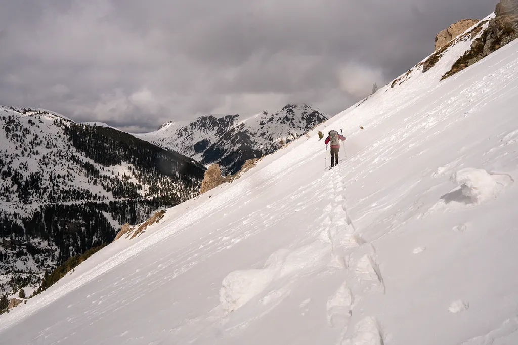 Een wandelaar loopt een steile, besneeuwde berghelling op met ruige, besneeuwde bergtoppen op de achtergrond.