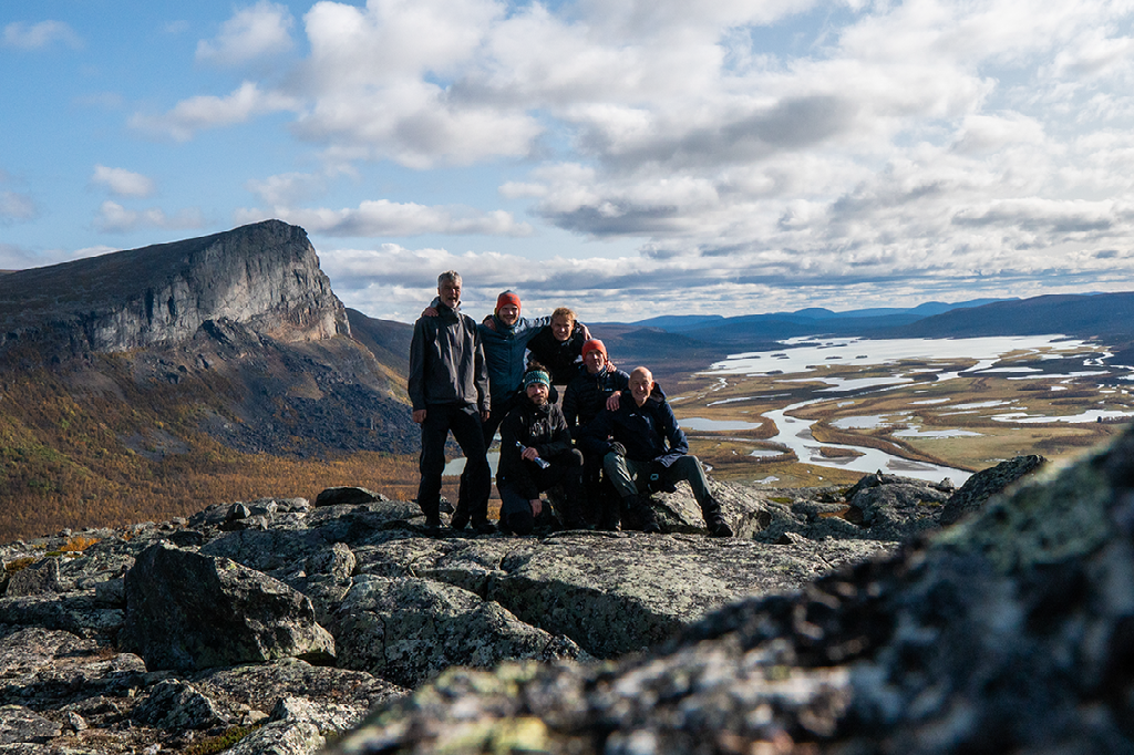 Een groep wandelaars zit bij elkaar op een rotsachtige berghelling met een weids uitzicht over de rivierdelta van de Rapa-vallei en bergen op de achtergrond.