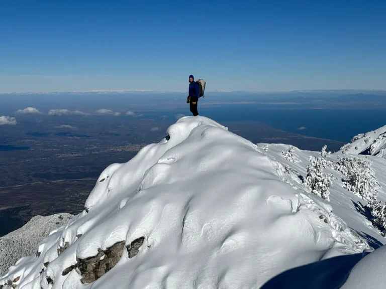 Wandelaar op besneeuwde bergtop met panorama over Olympus