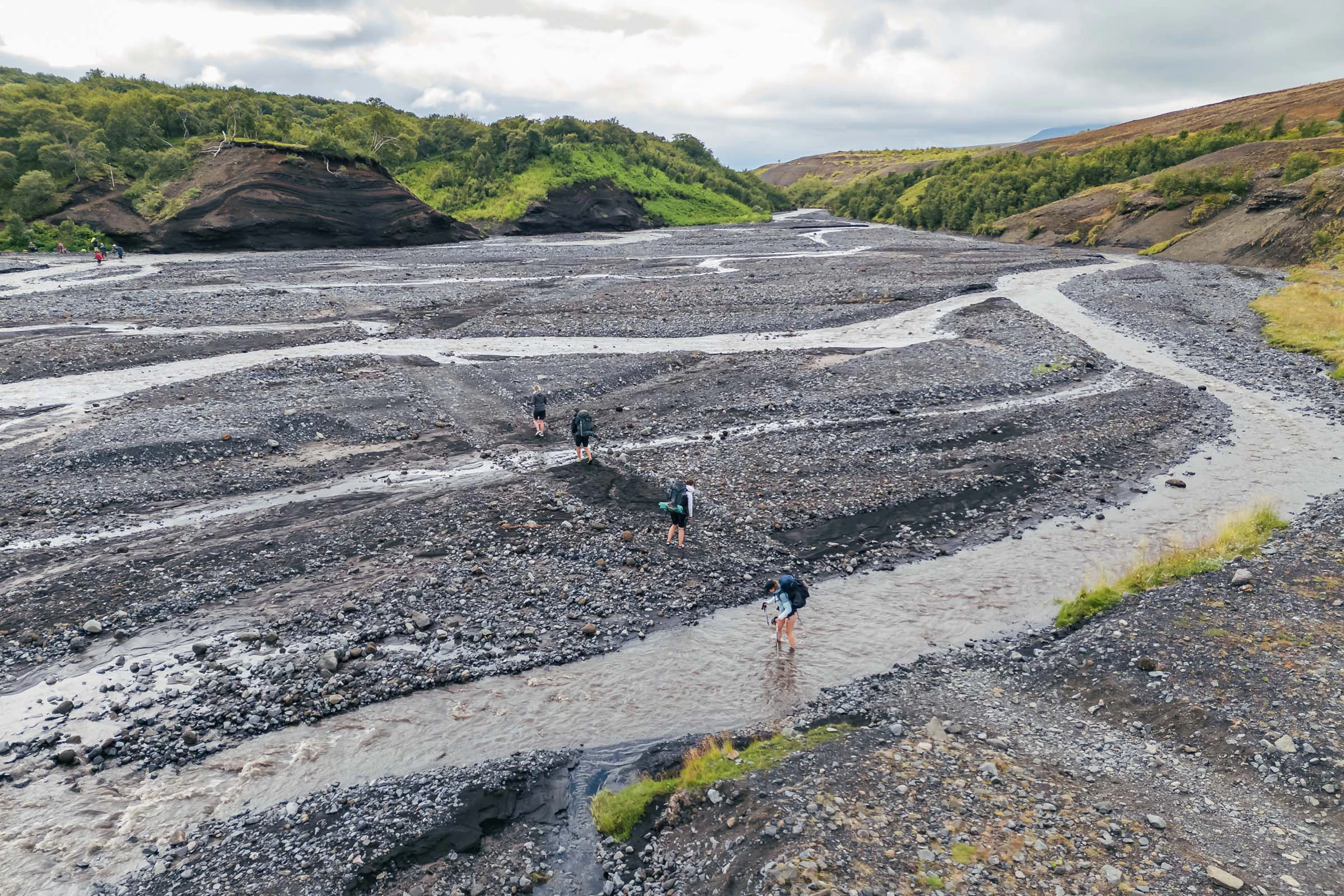 Wandelaar steekt een rivier door een stenige vlakte over