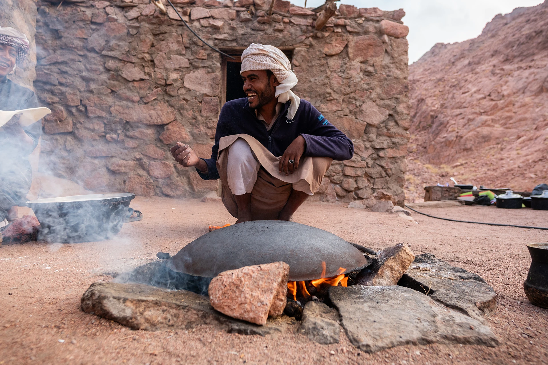 Man zit gehurkt bij stenen vuurplaats