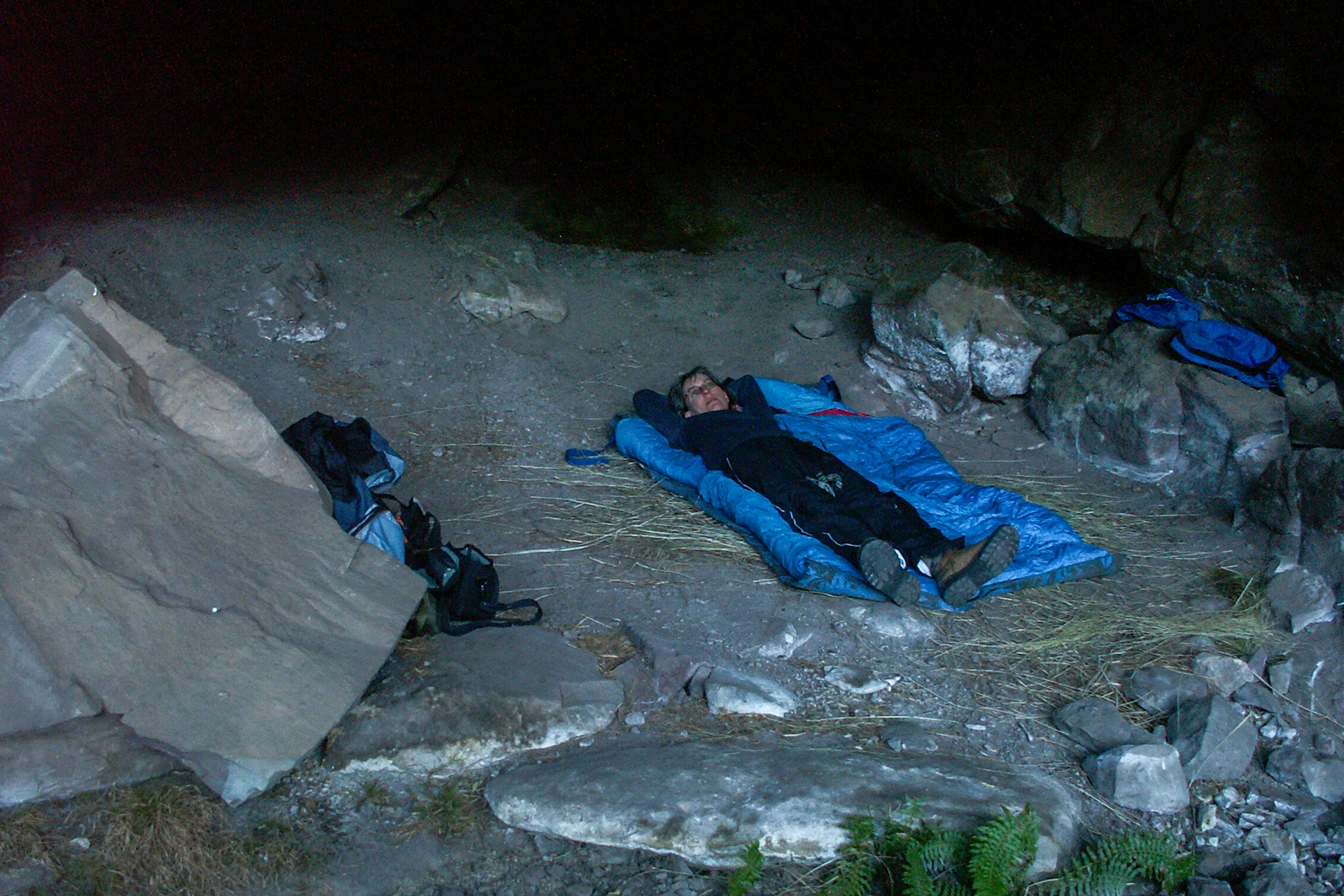 Kampeerder ligt in slaapzak onder een rots