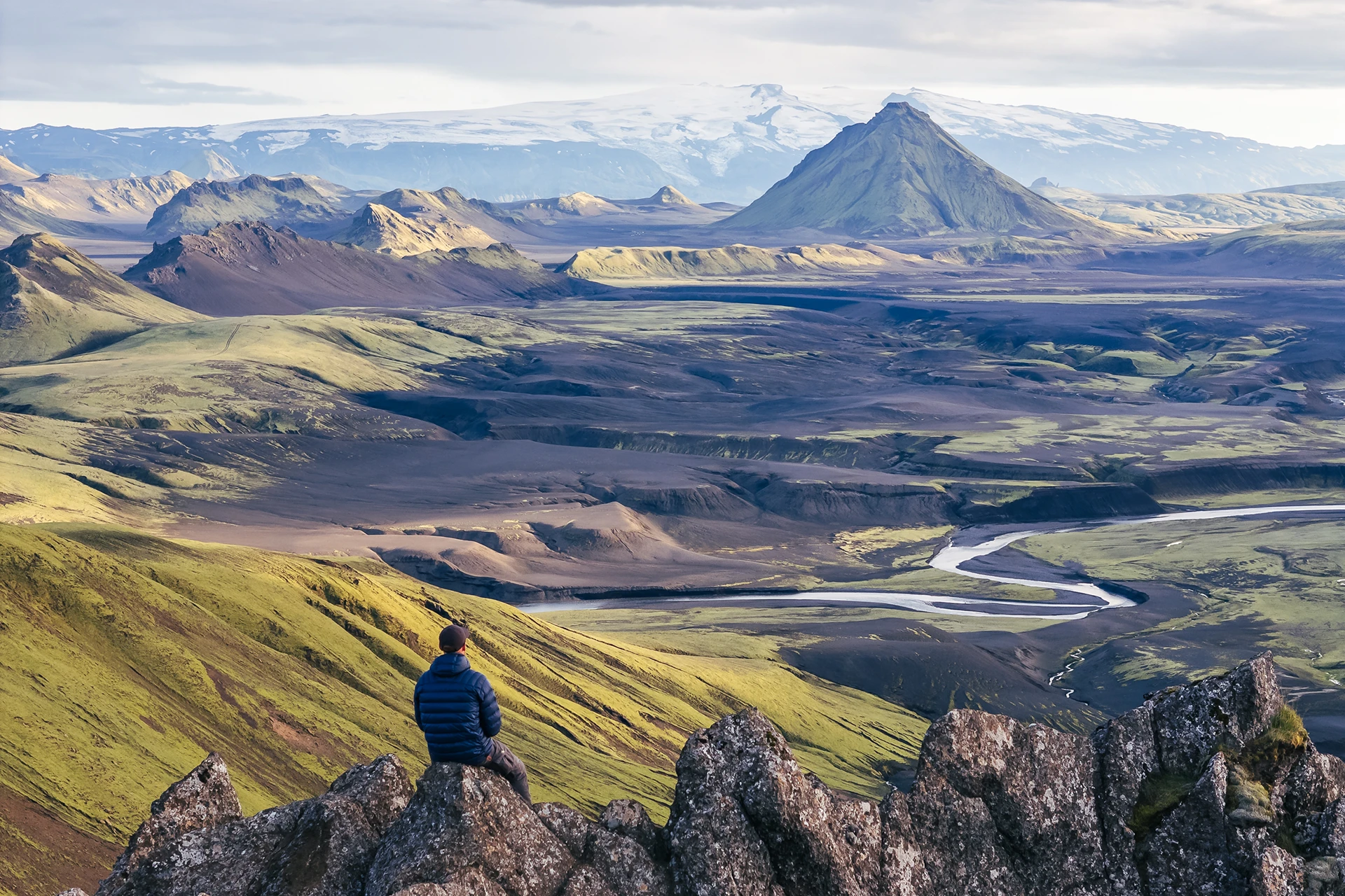 Wandelaar zit op een rots met uitzicht op vulkanisch landschap