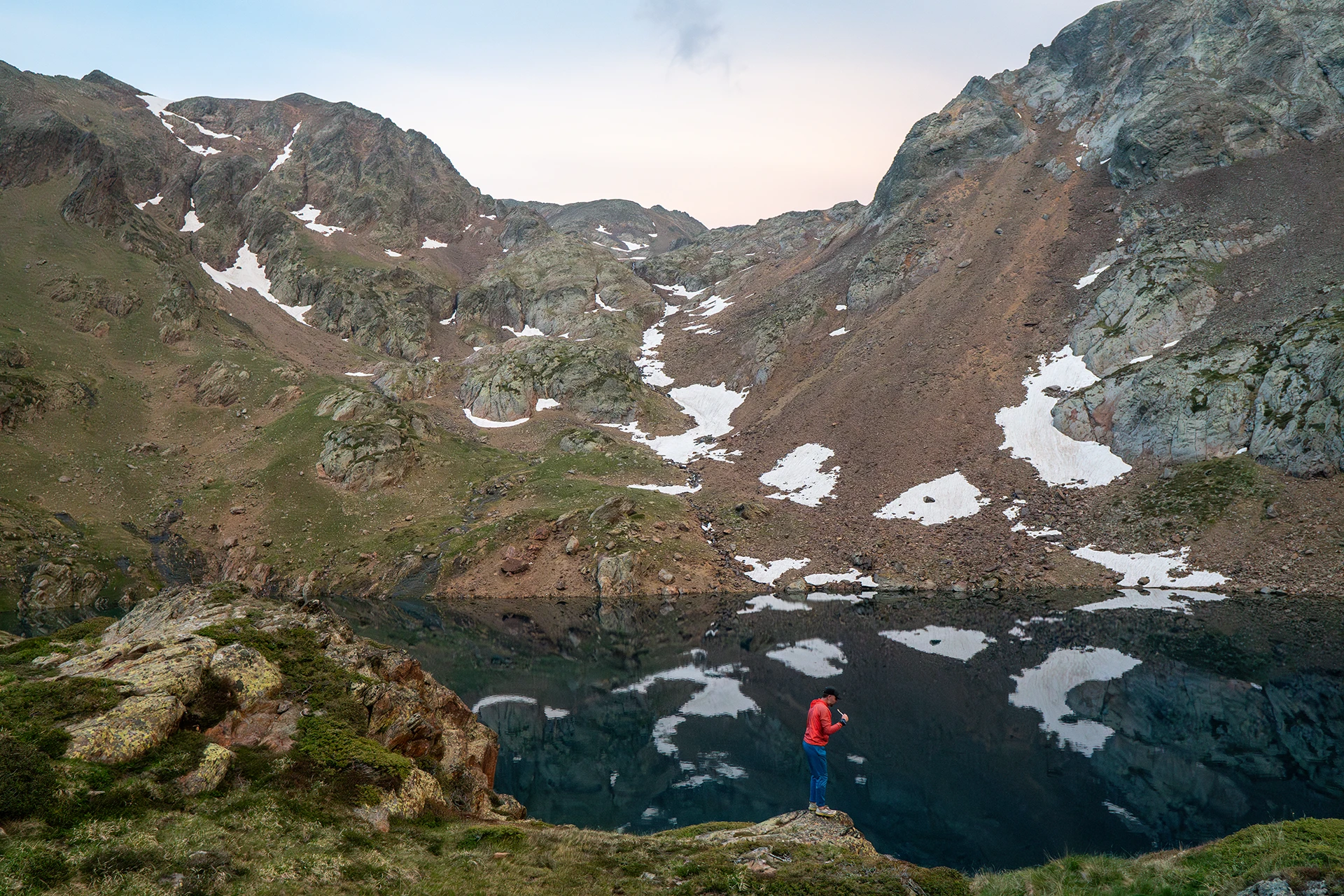 Bergmeer met rode tent op rotsige oever