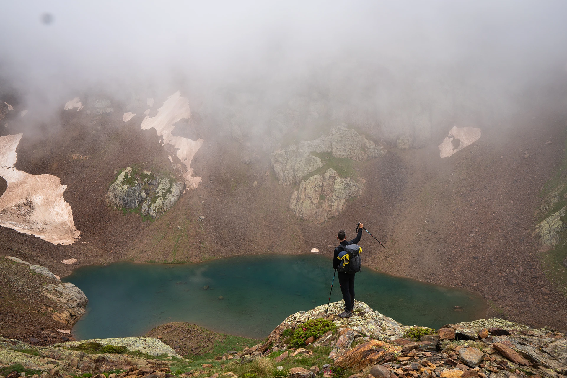 Wandelaar staat bij mistig bergmeer tussen rotsen