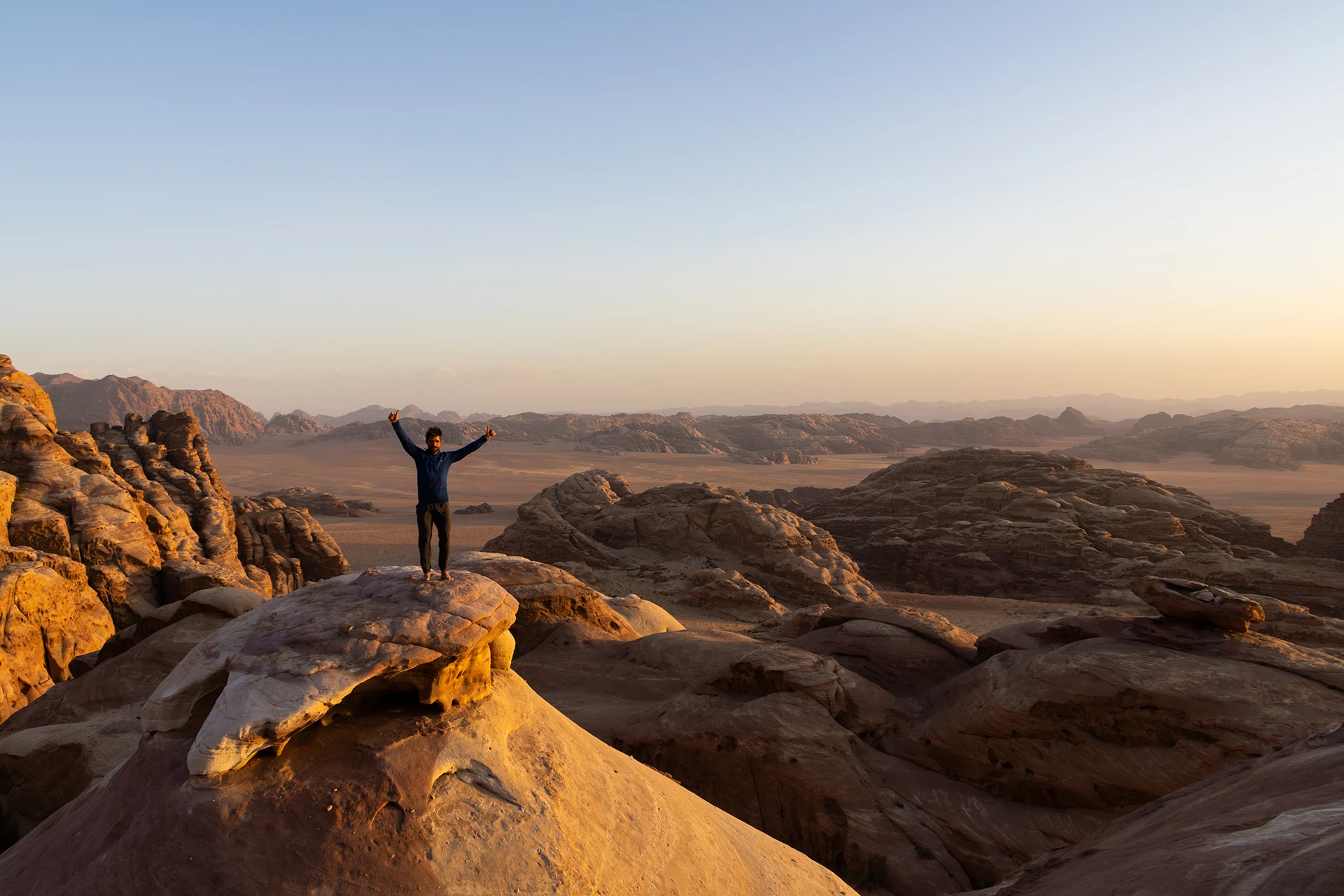 Wandelaar met open armen op rots bij zonsondergang