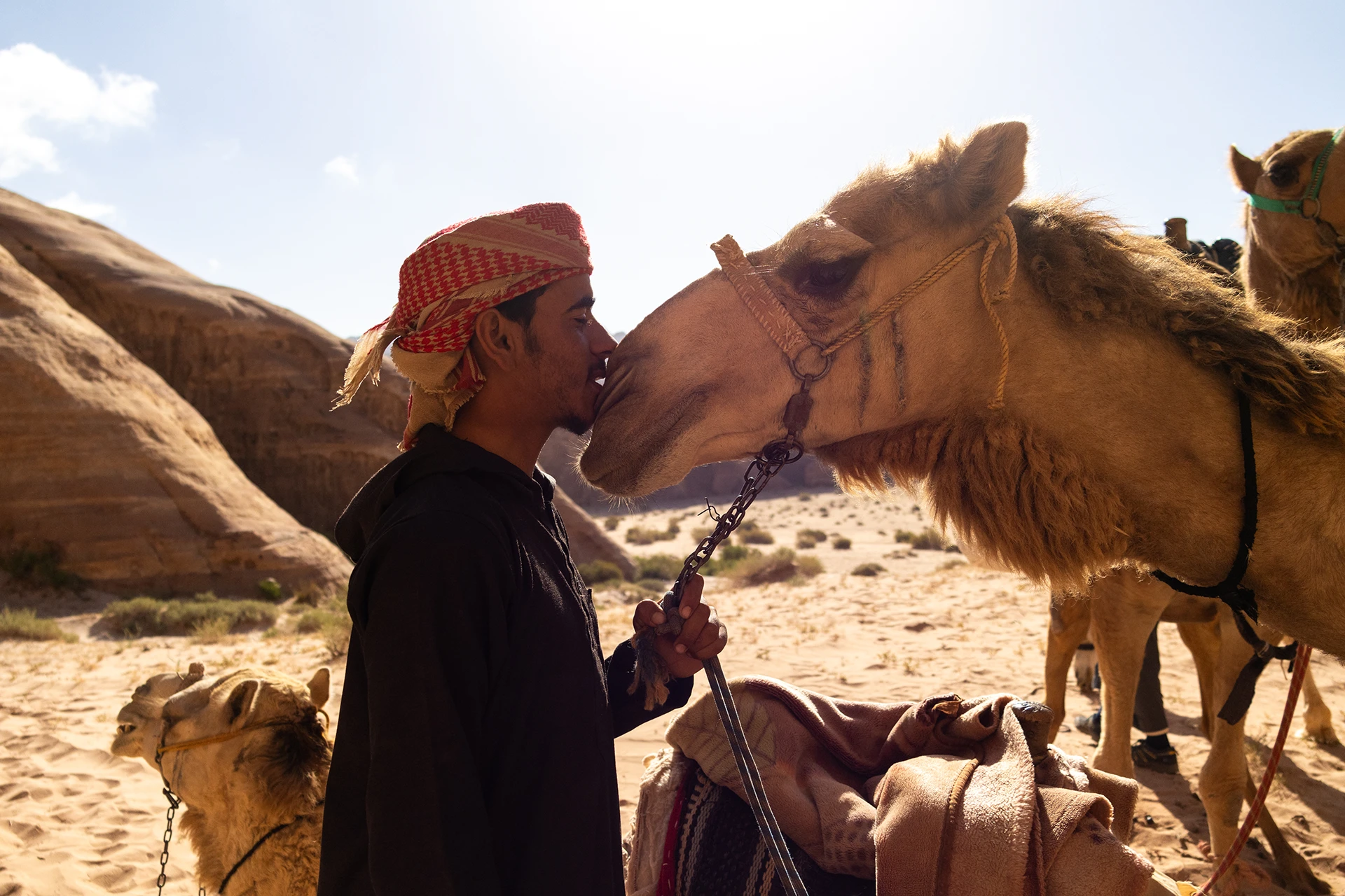 Man staat met kameel tegen oranje rotswand