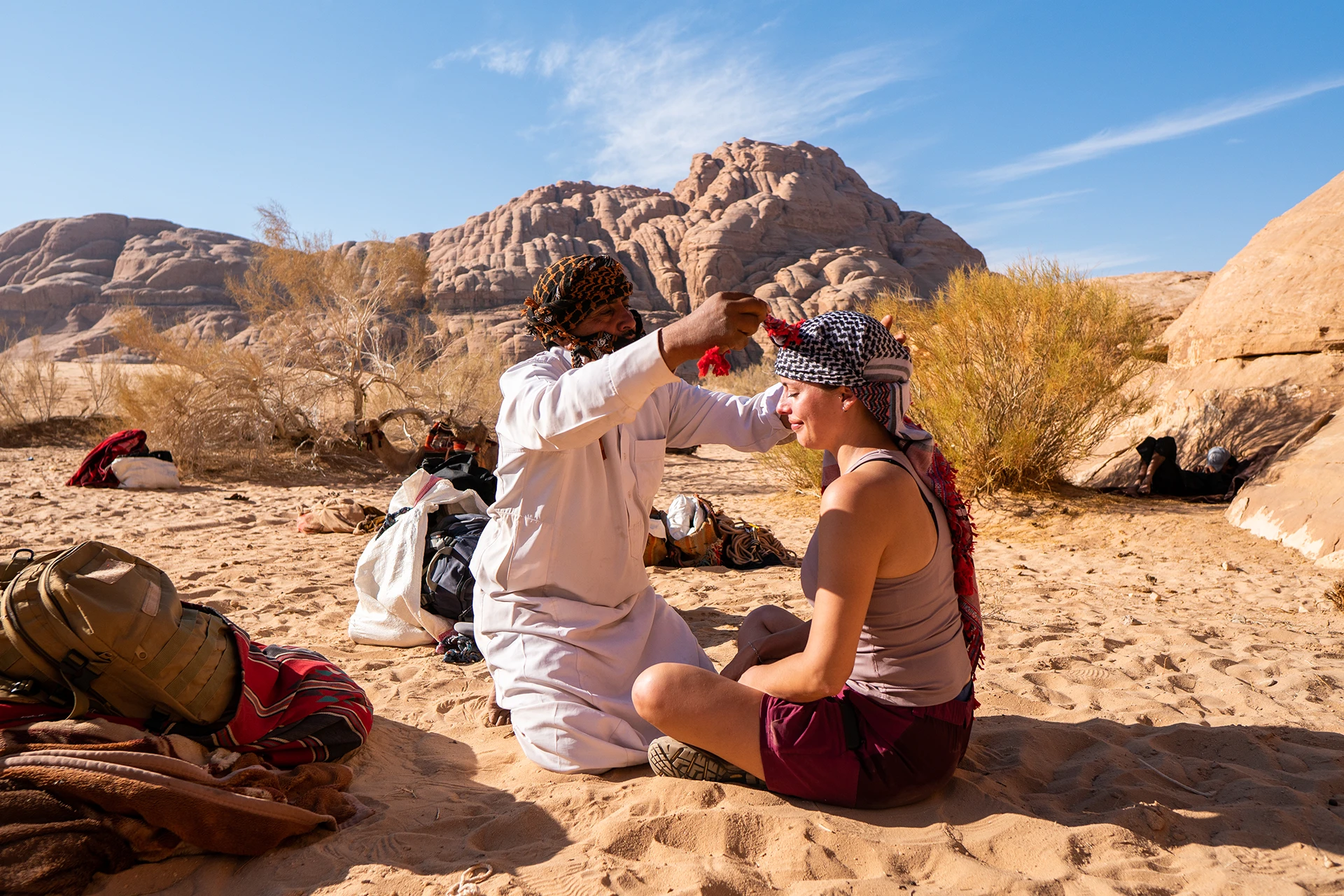 Vrouwen zitten pratend in het zand bij struiken