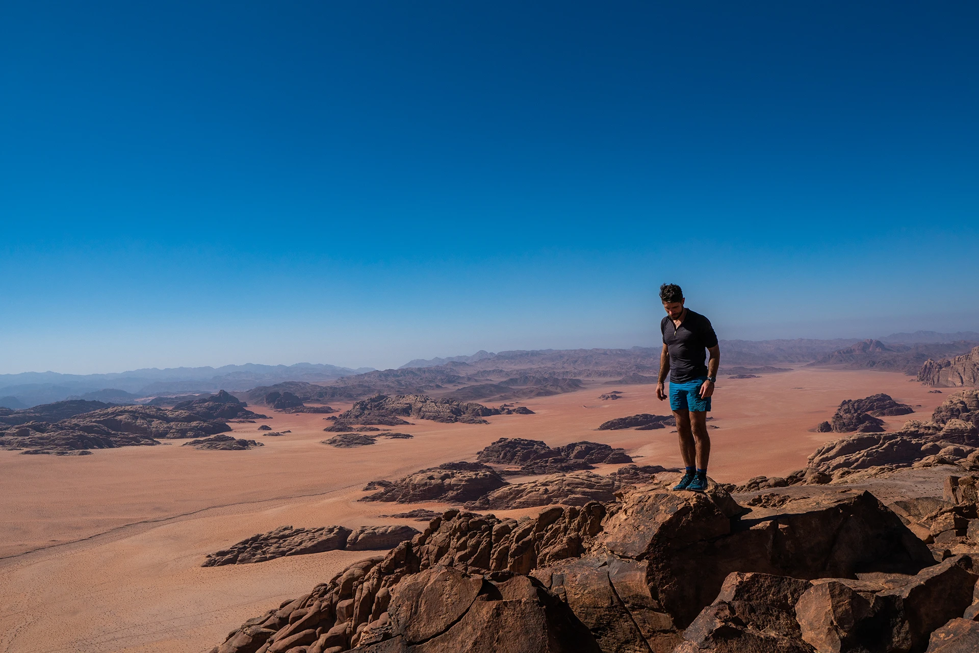 Wandelaar staat op rots met uitzicht op wijd woestijnlandschap
