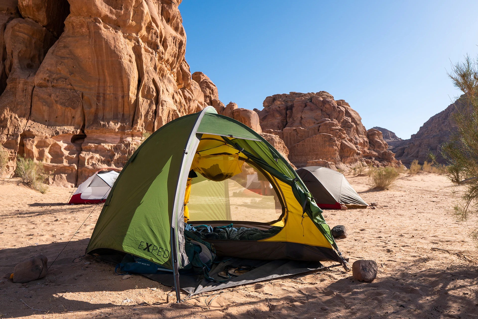 Groene tent staat tussen rotsen in een woestijnkamp