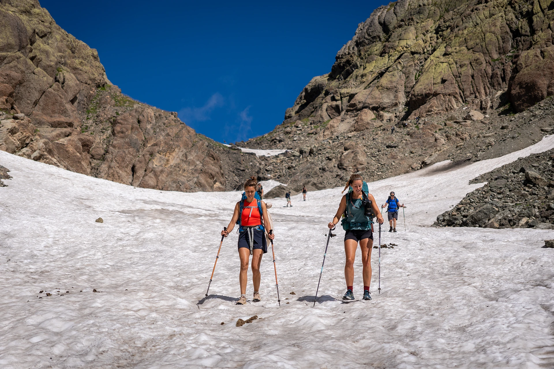 Twee wandelaars staan op sneeuwveld tussen rotsen