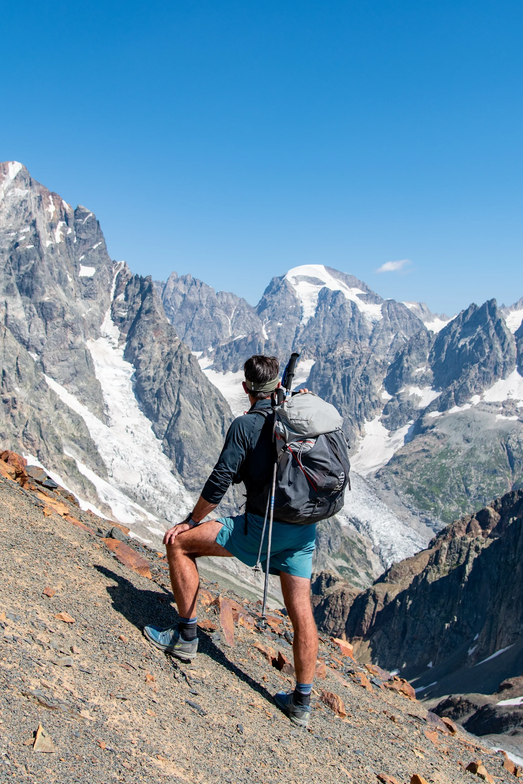 Wandelaar staat op rotsrand met uitzicht op besneeuwde pieken