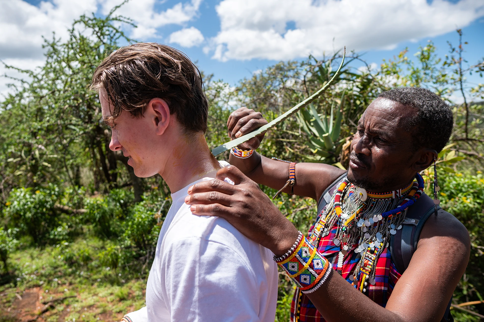 Persoon die een kralenketting omdoet bij een reiziger in een bosrijk gebied