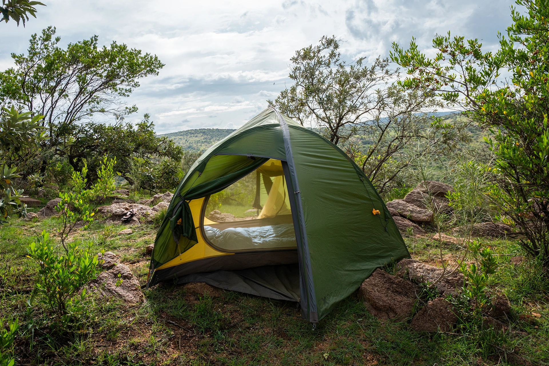 Kleine groene tent opgezet tussen struiken met heuvels op de achtergrond