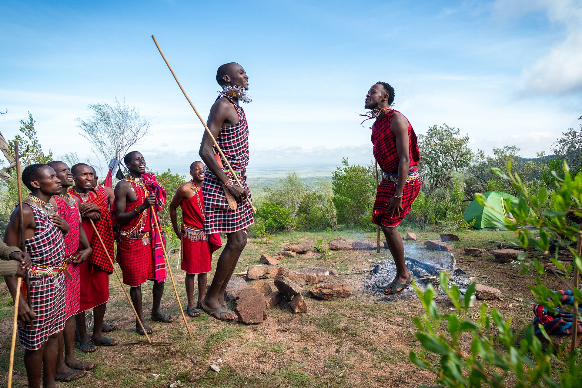 Groep Maasai kinderen die buiten spelen met een volwassene die iets demonstreert