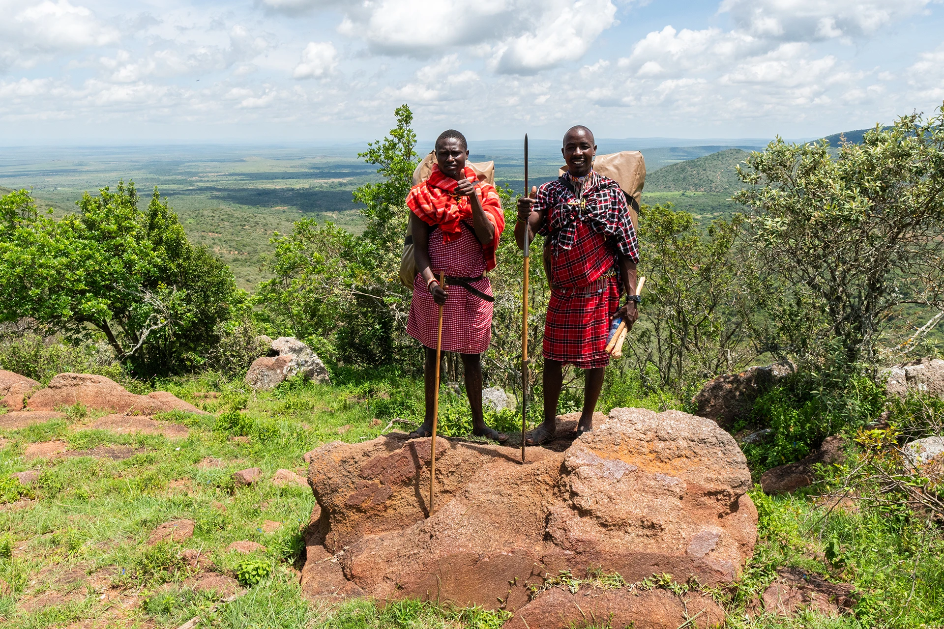 Twee mannen in traditionele kleding staan op rotsblok met groene vallei achter