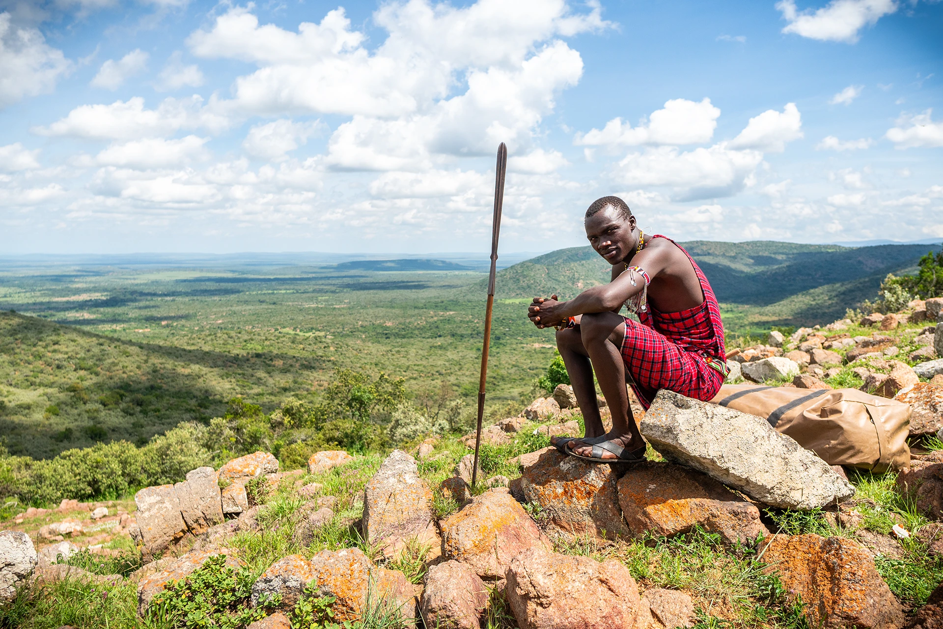 Man in rode kleding zit op rots met uitzicht over uitgestrekt groen landschap