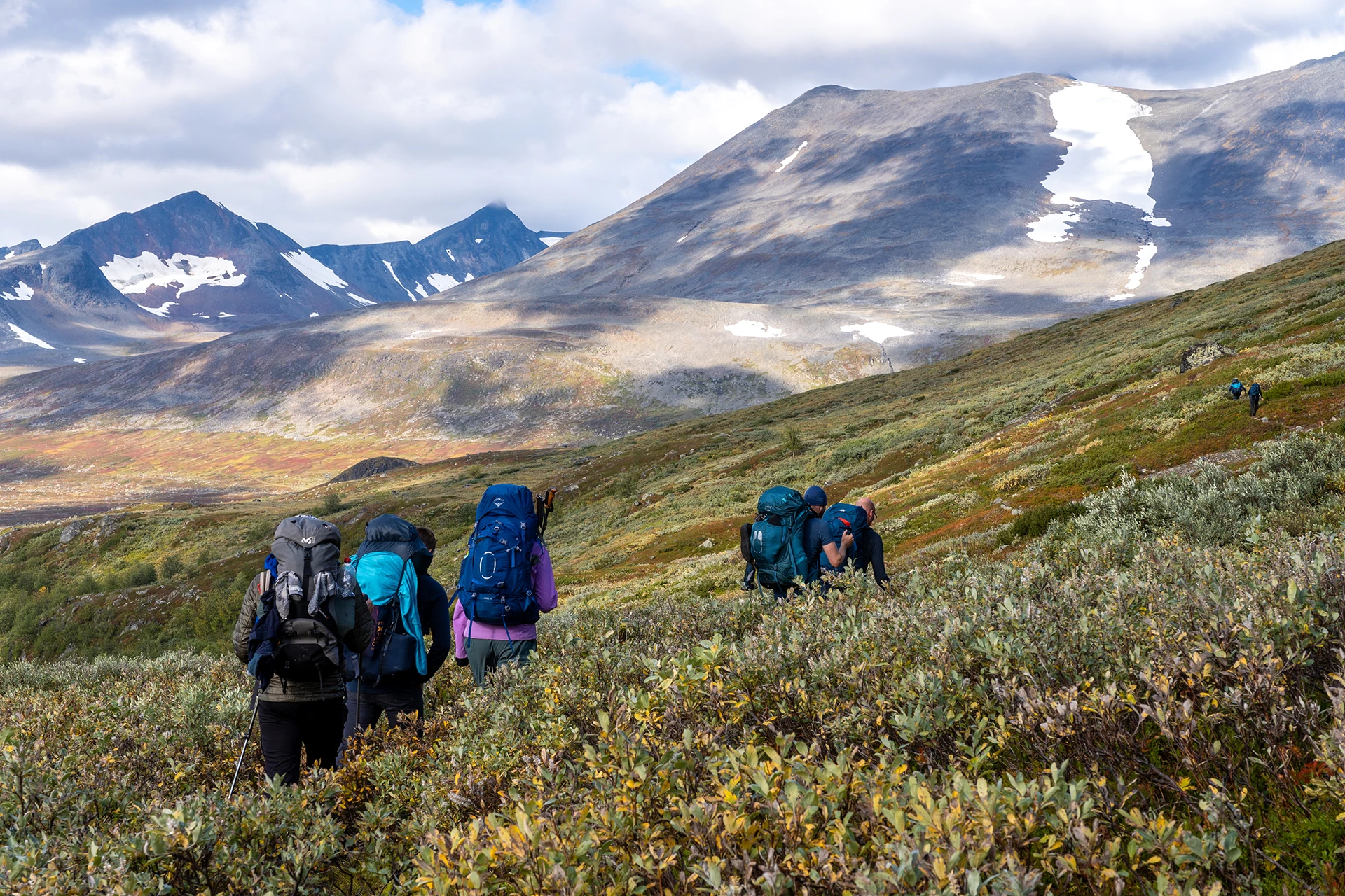 Wandelgroep die over lage struiken loopt richting een vallei