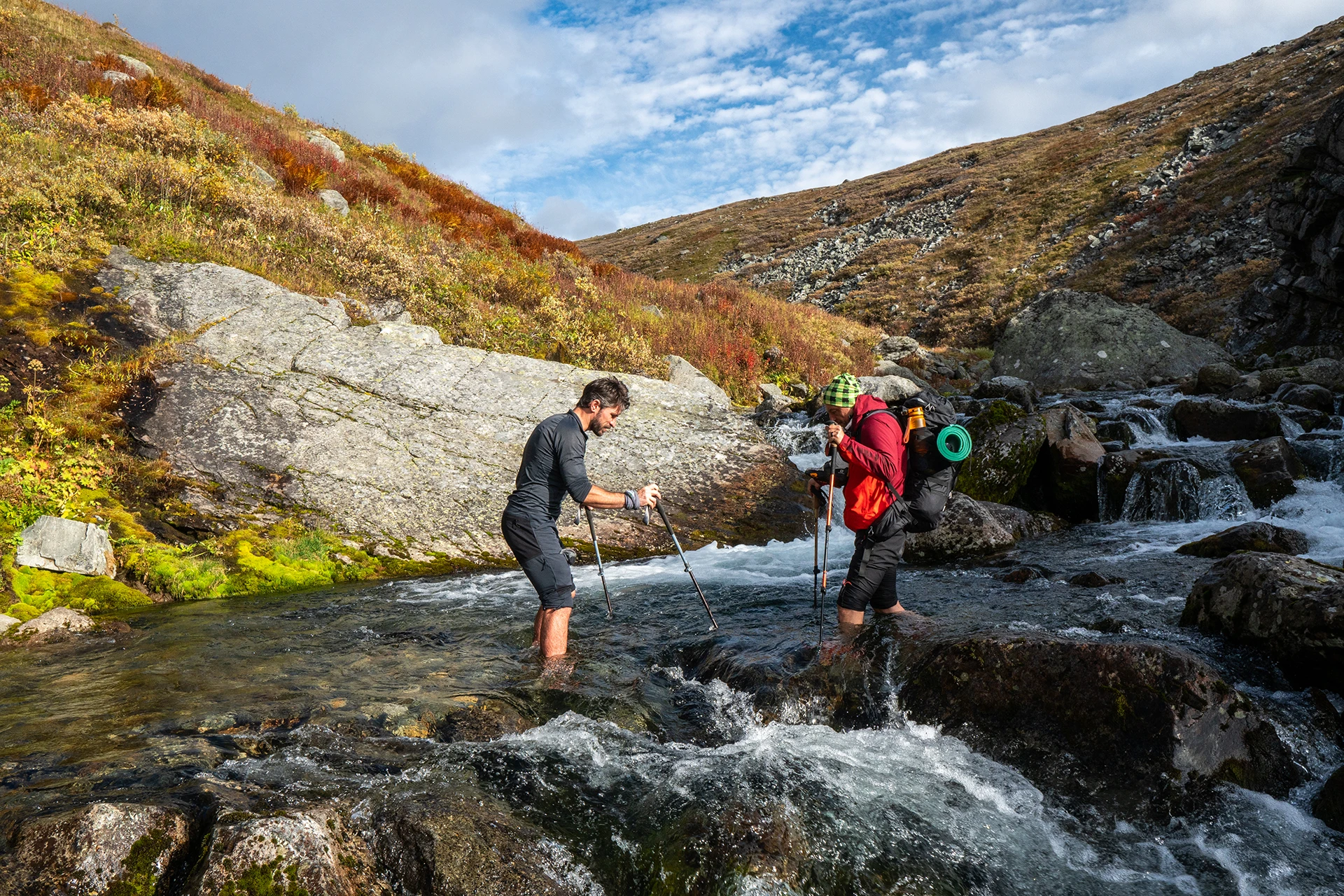 Twee wandelaars die elkaar helpen bij een beekje op een rots