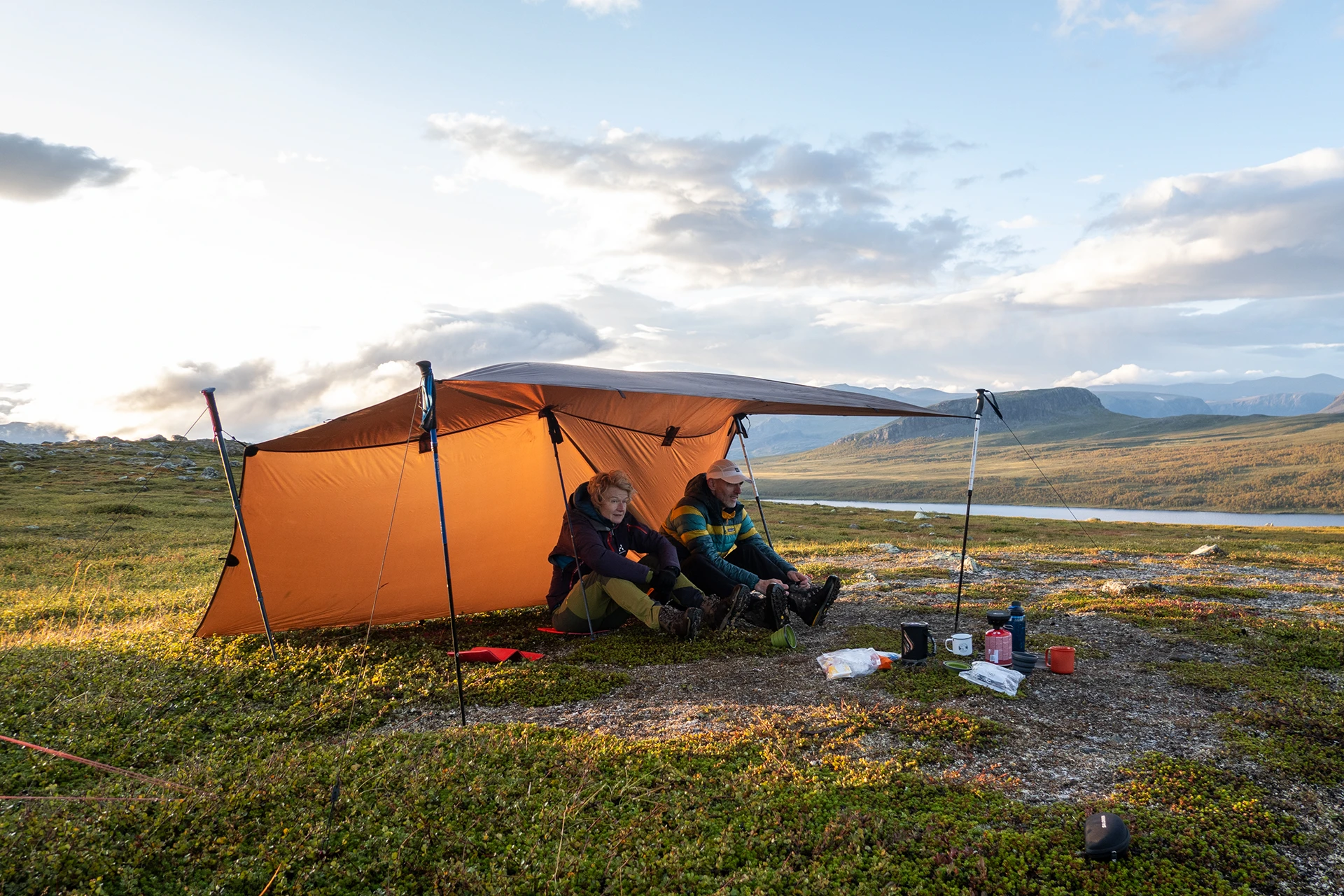 Oranjerode tarp met kampeerders die koken en uitrusten