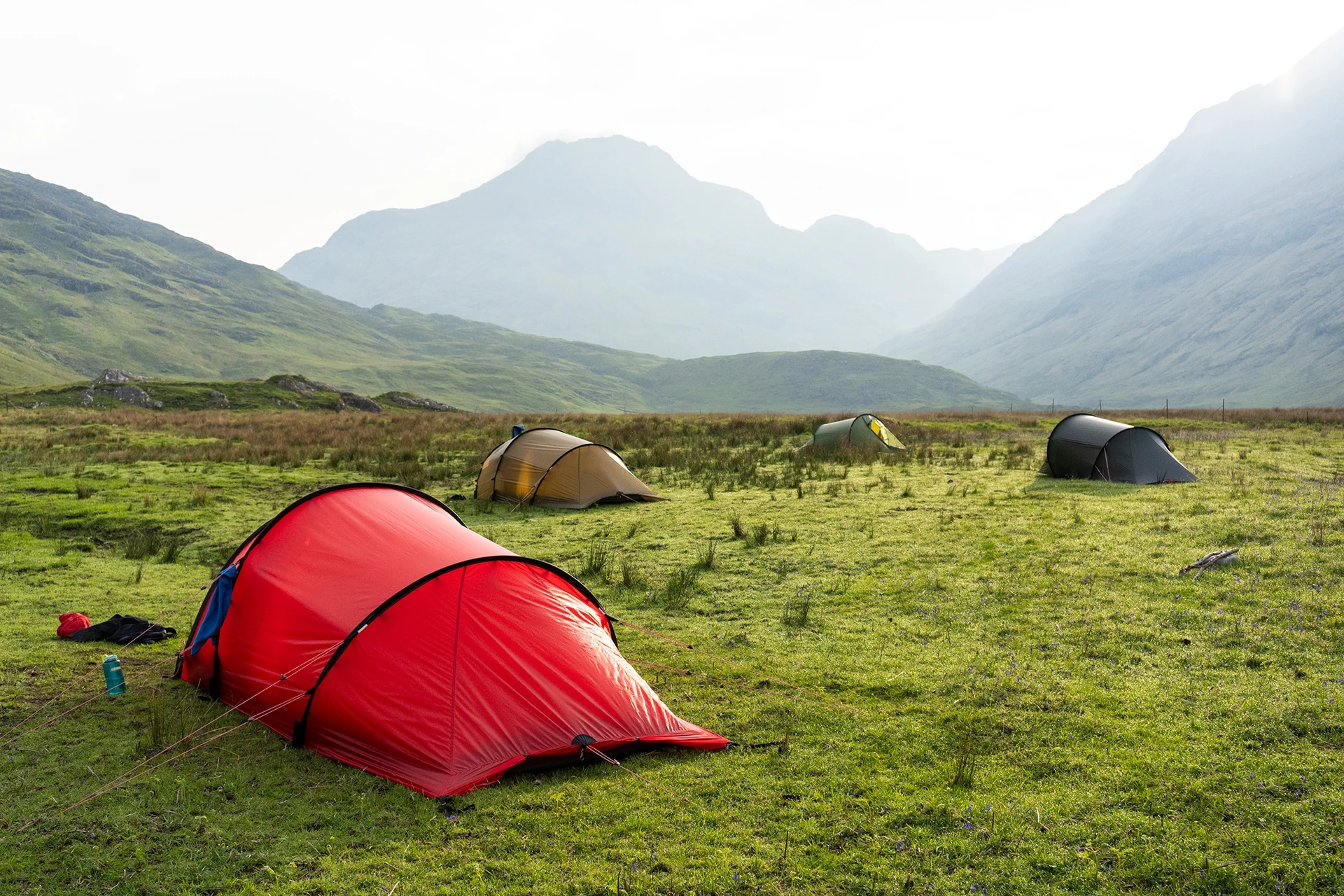 Rode tenten op een groene weide met mistige bergen op de achtergrond