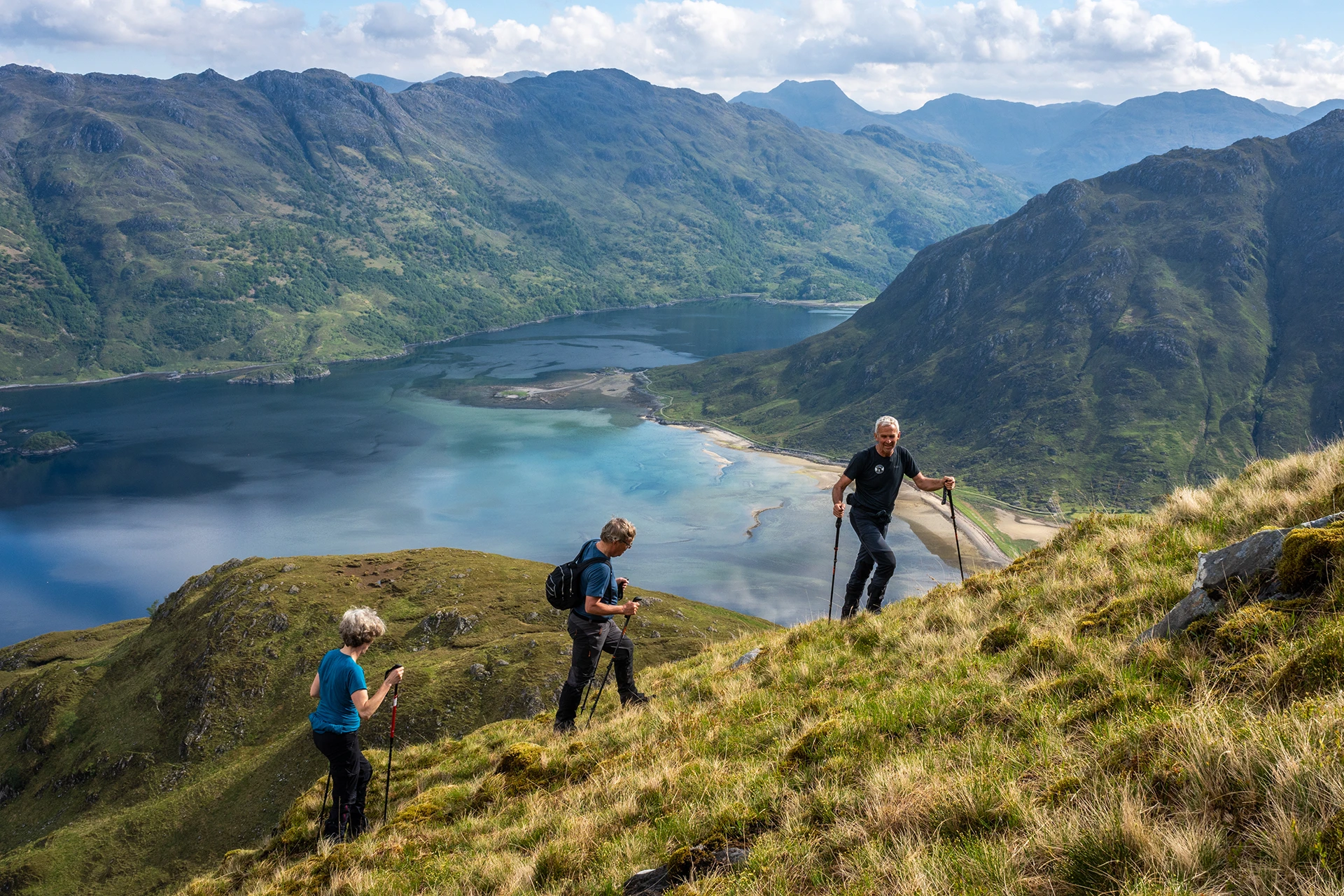 Drie wandelaars die over een hoge bergkam lopen met valleien onder zich
