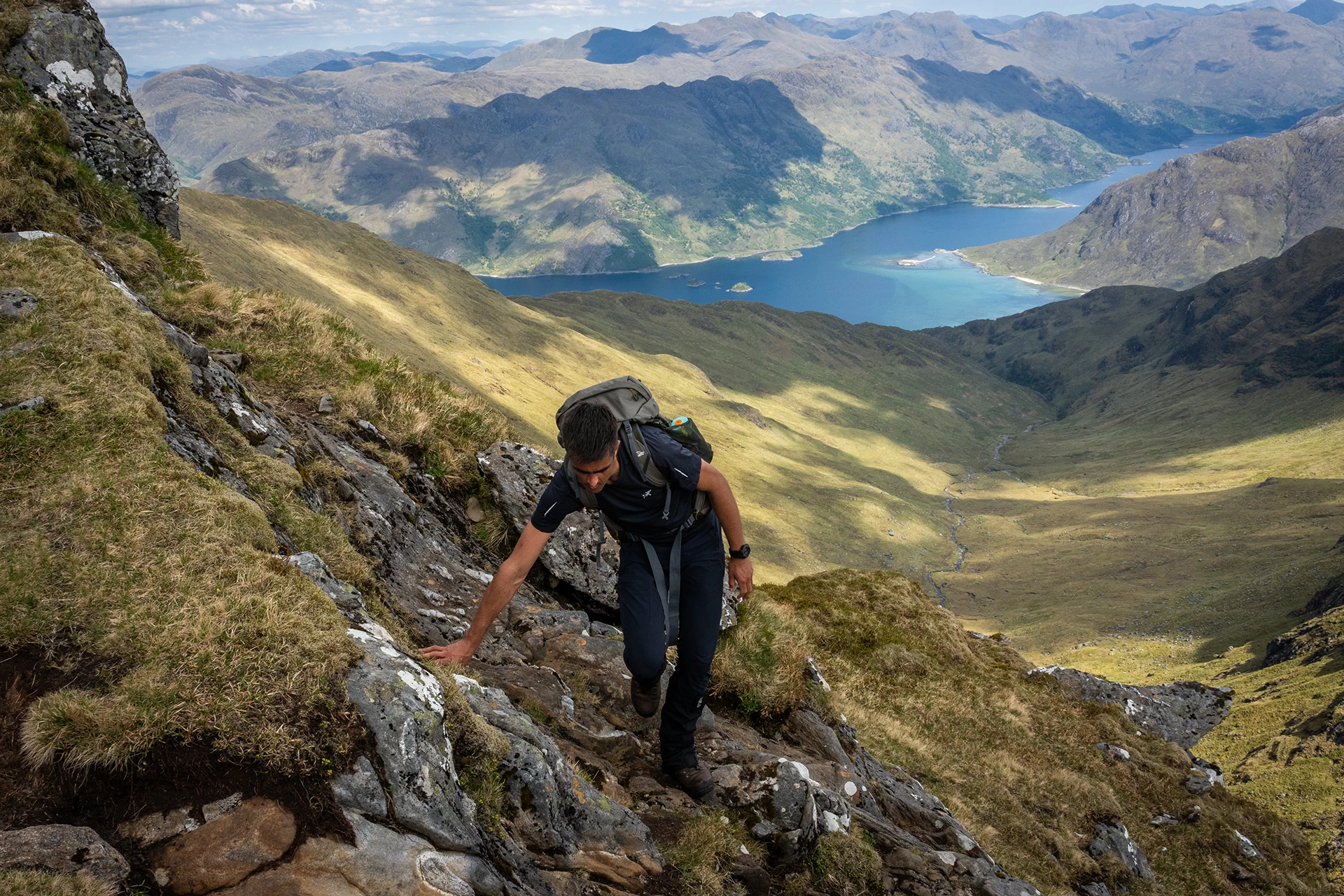 Hiker die een rots beklimt boven een diep dal met blauw water
