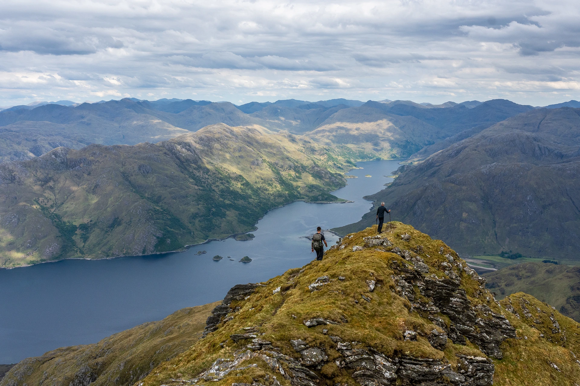 Wandelaar die langs een steile berghelling loopt met uitzicht over een meer