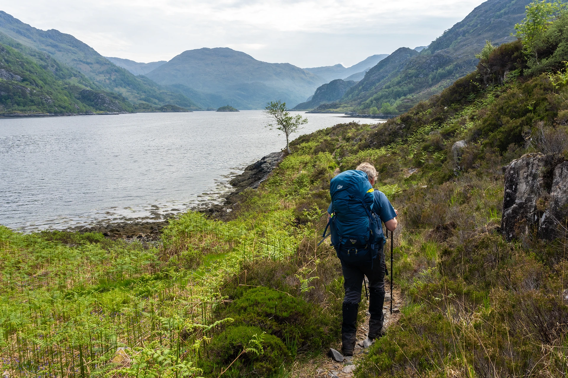 Hiker die langs een meer loopt met bergen op de achtergrond