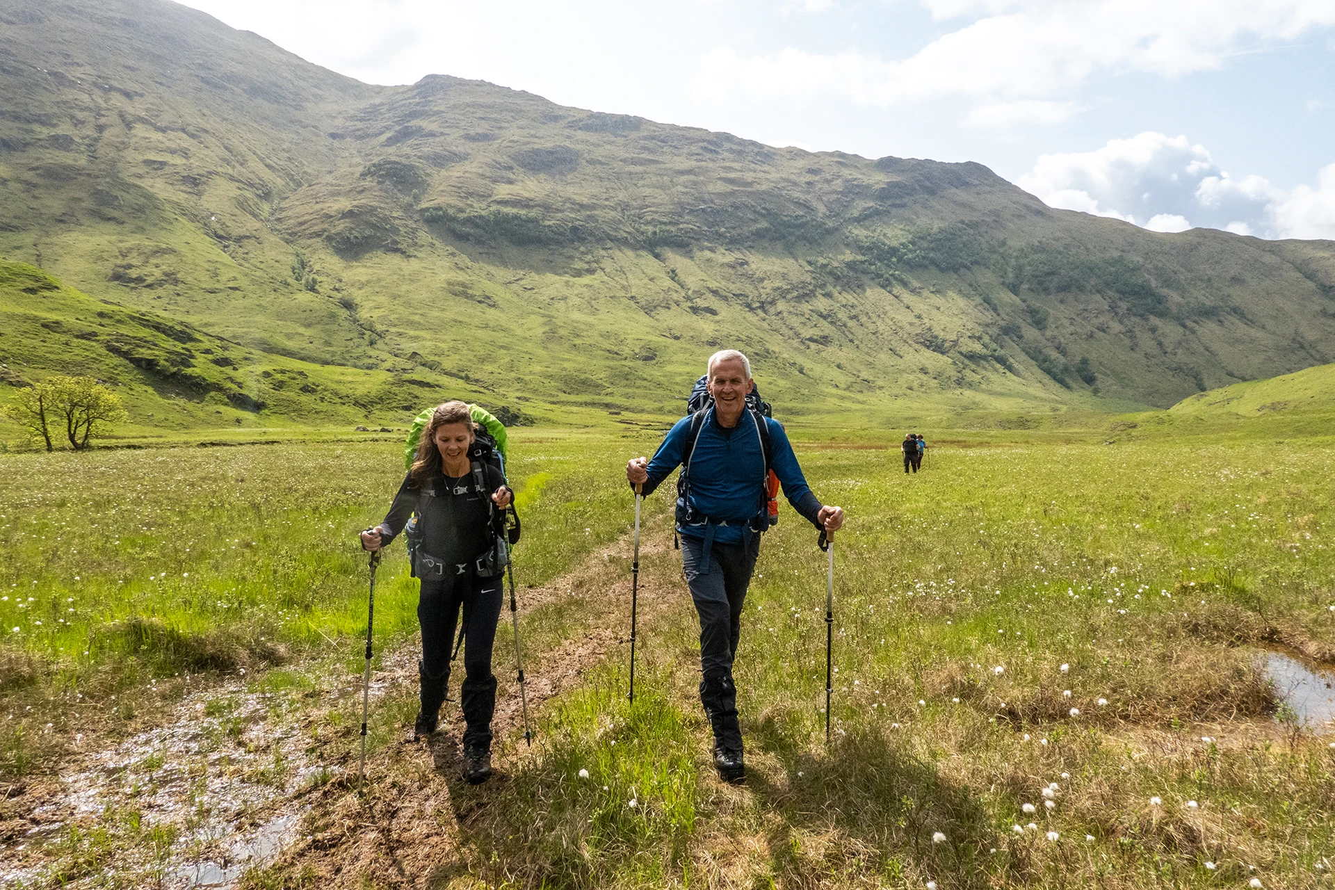 Twee wandelaars in een open groen landschap met mistige bergen