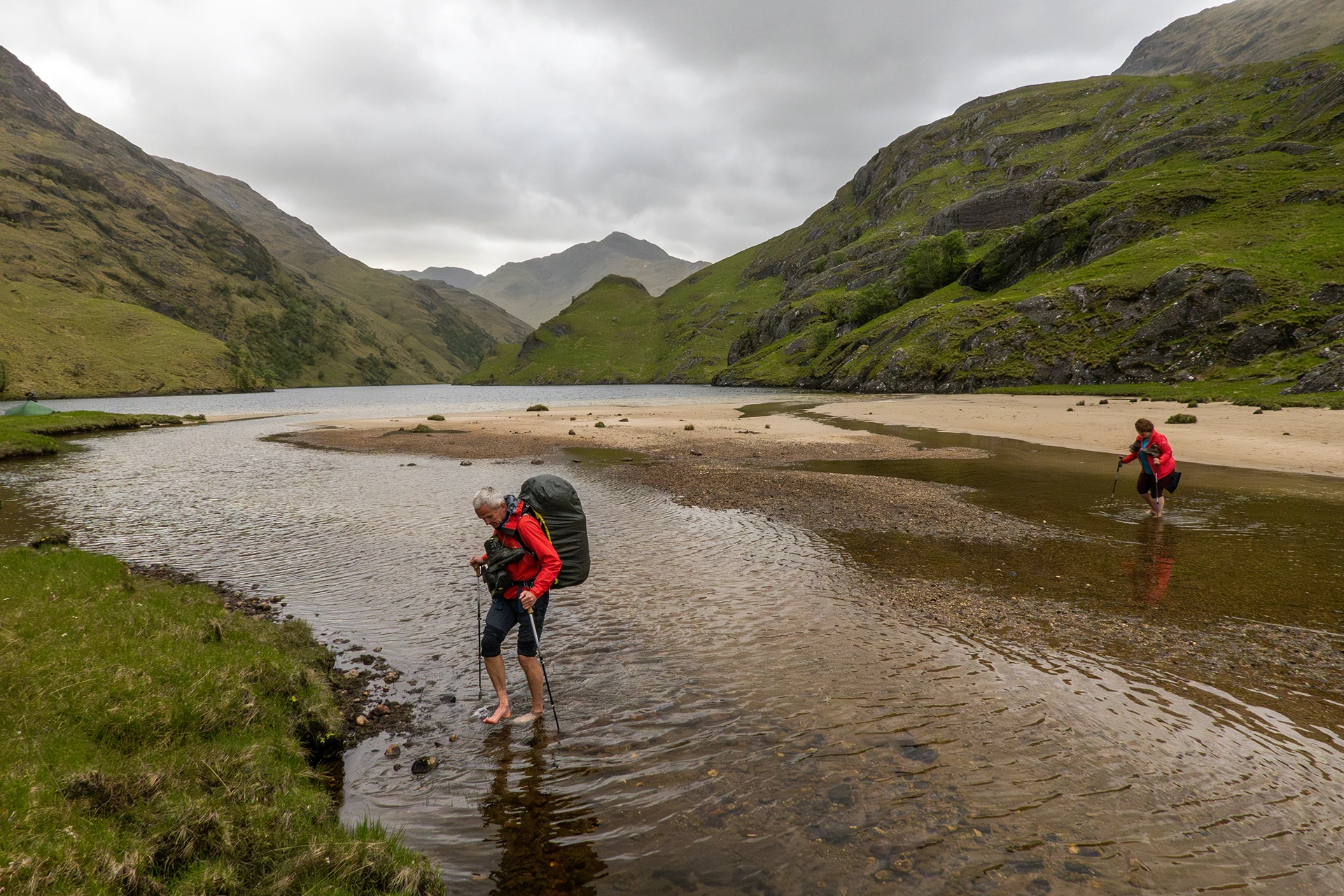 Hiker die door een ondiepe rivier loopt in een brede vallei