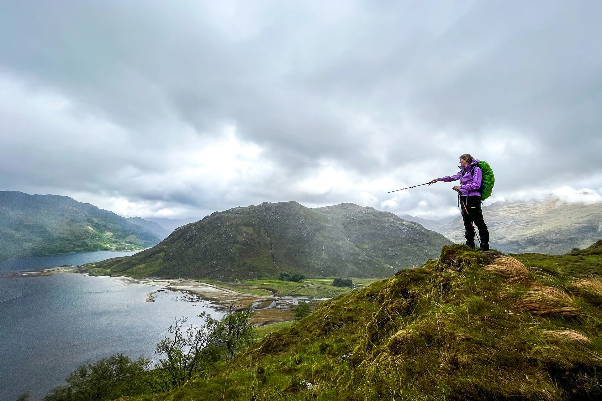 Hiker die bij een meer op een berghelling naar het uitzicht kijkt