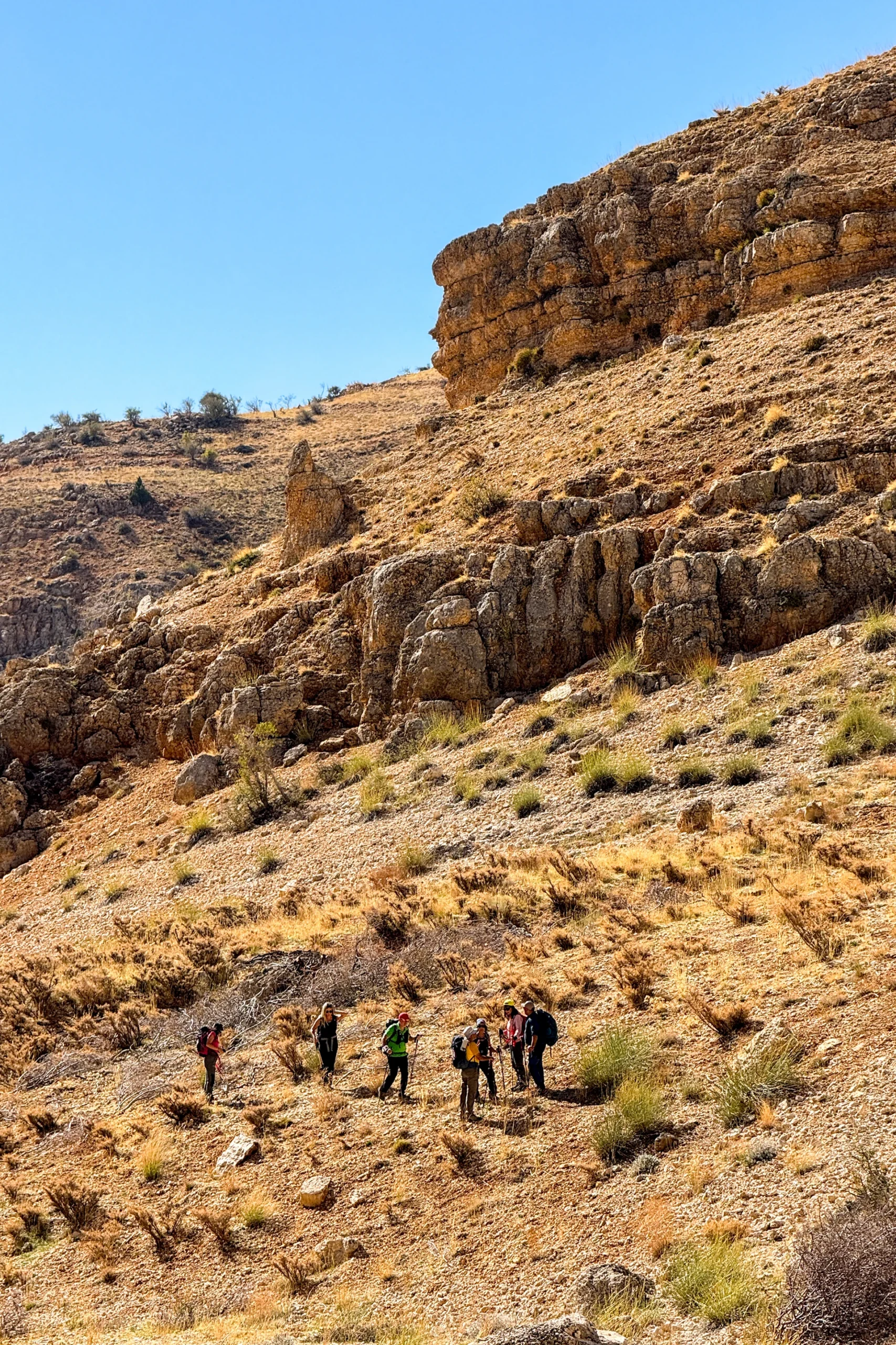 Wandelgroep die langs een rotswand door een droge vallei trekt