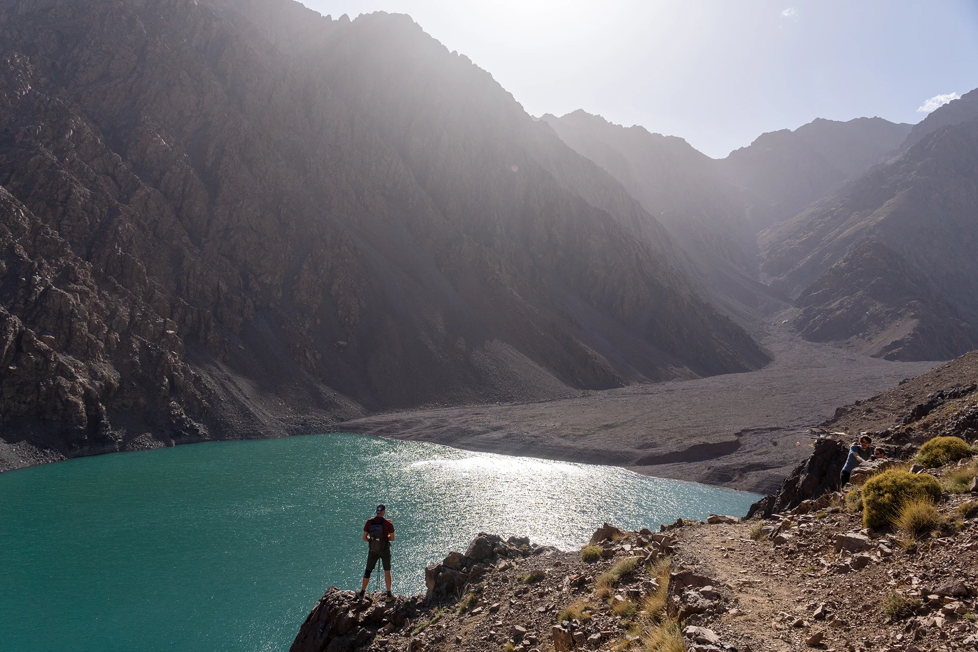 Wandelaar die bij turquoise water tussen hoge bergen staat