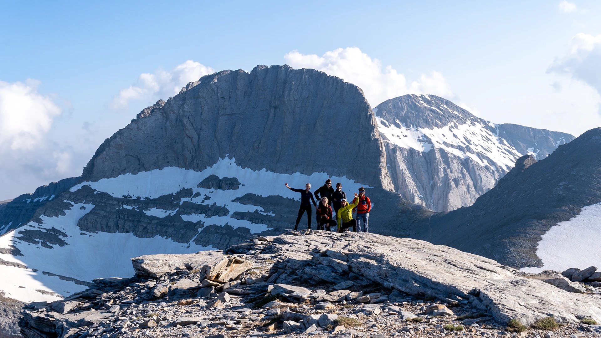 Hikers op een brede steenplaat met hoge besneeuwde bergwand