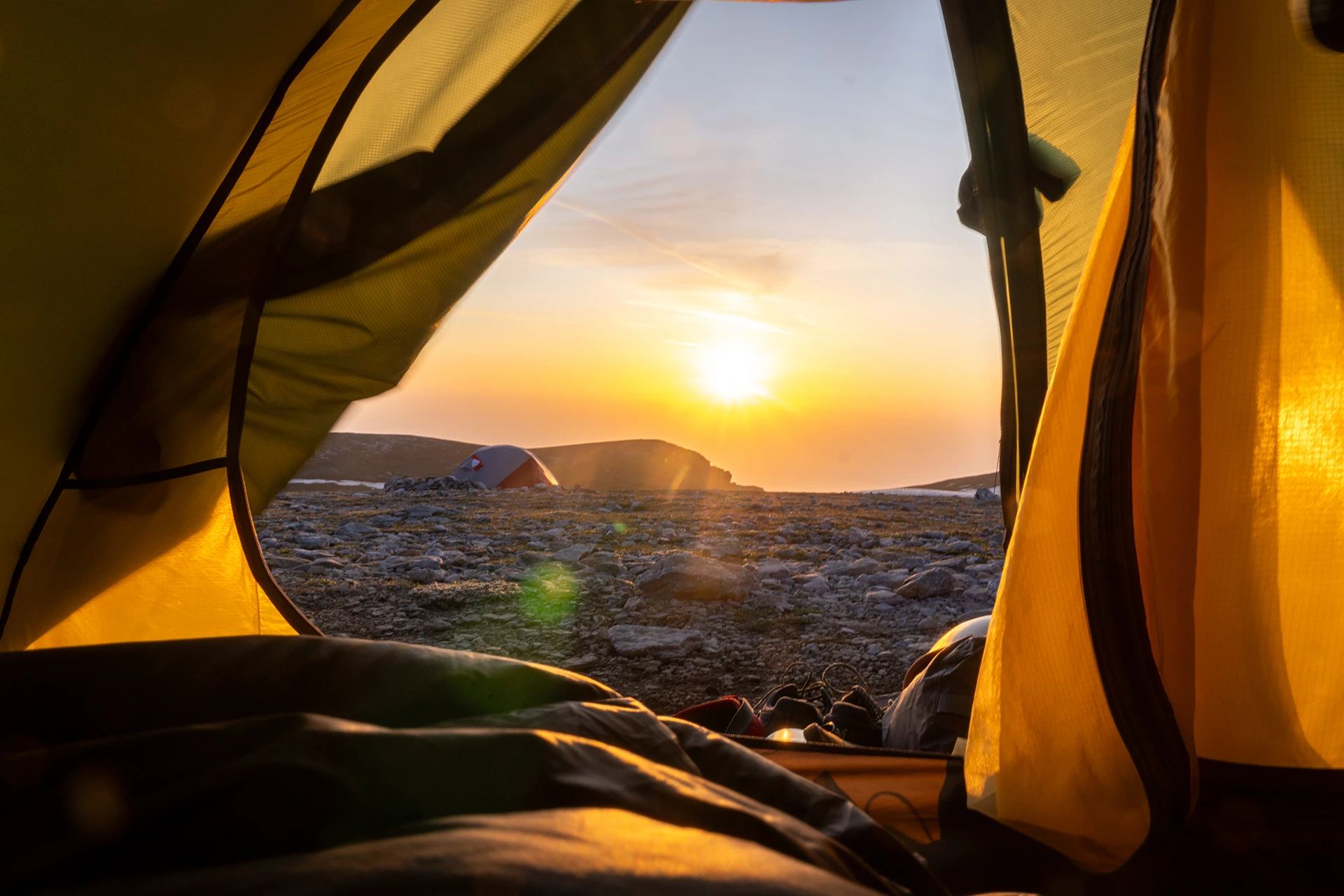 Zonsondergang met tenten op een rotsige vlakte