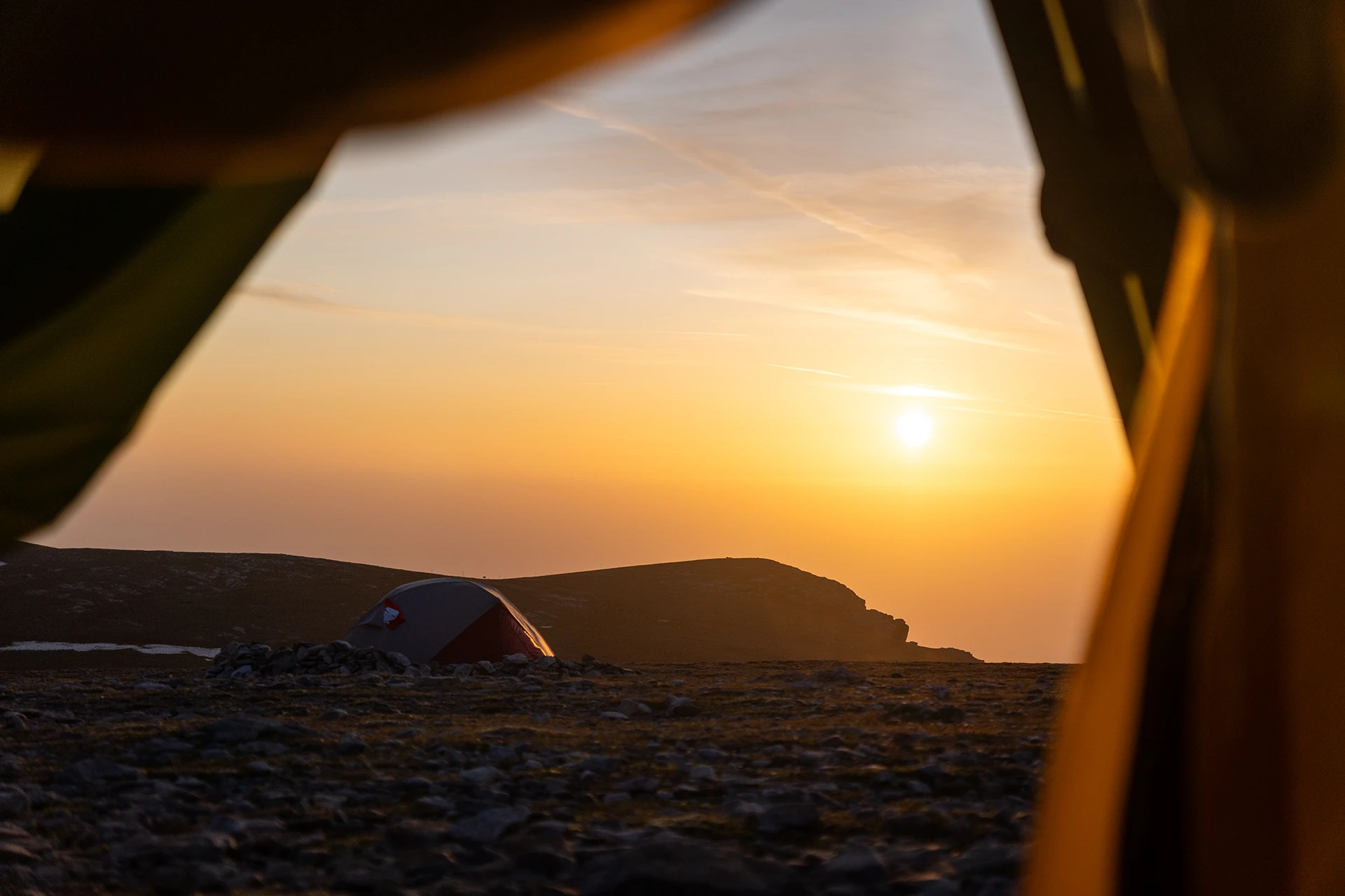 Zonsondergang gezien vanuit een tentopening op een hoog plateau