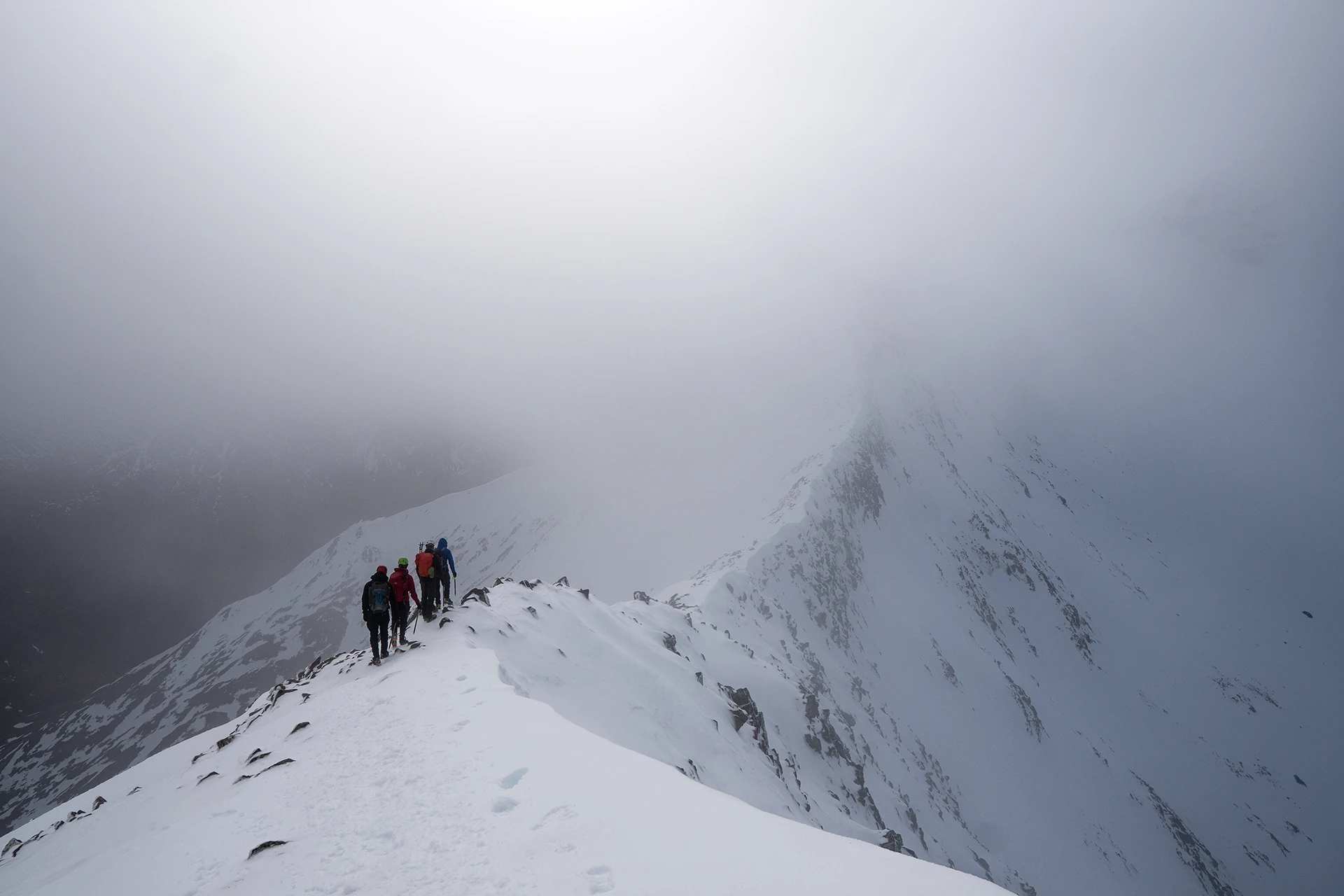 Groep klimmers die een smalle sneeuwgraat in mist beklimt