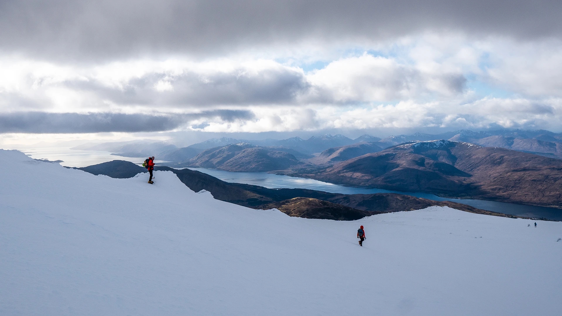 Wandelaar op een brede sneeuwrug met wolken boven de bergen