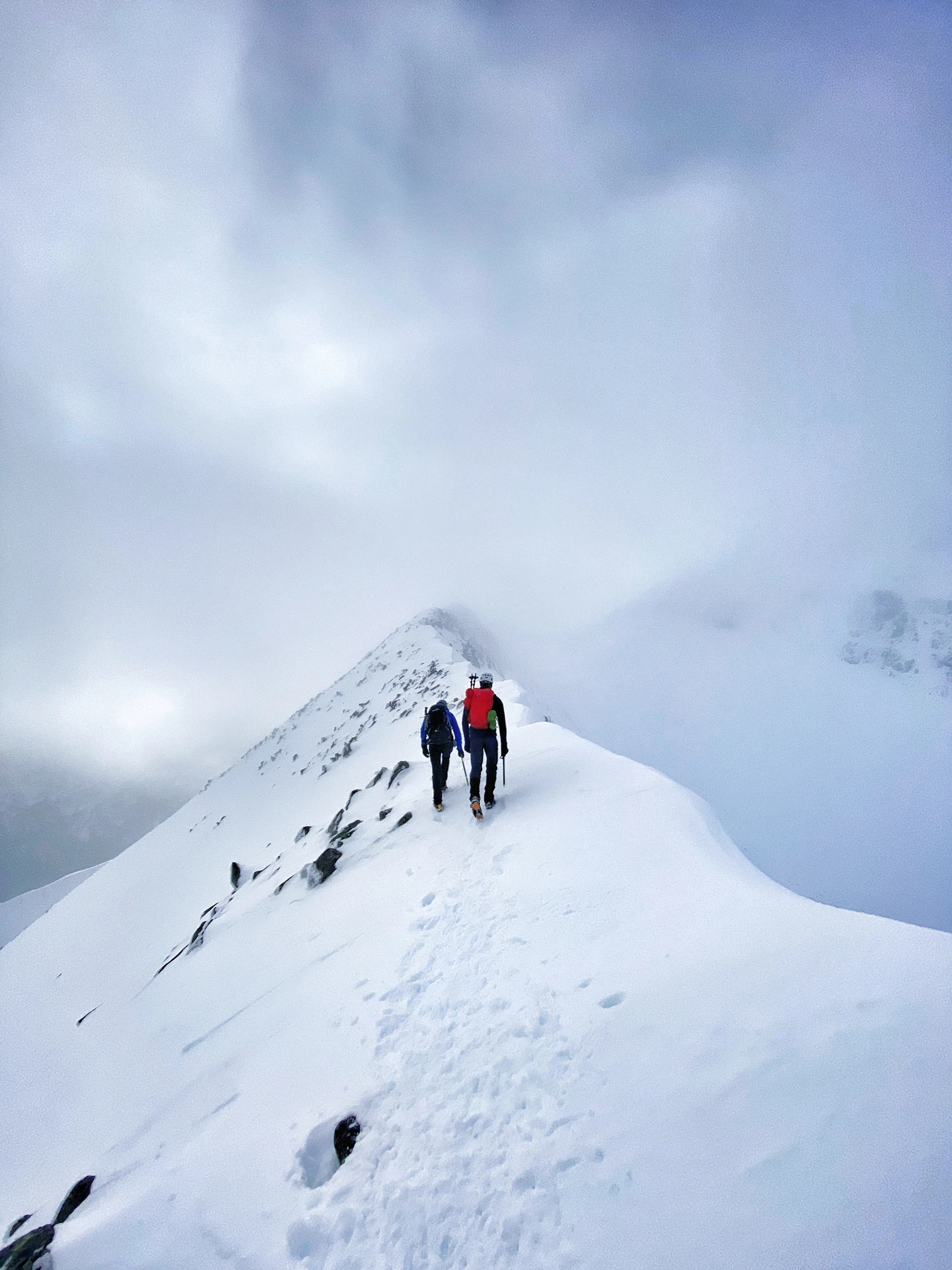 Twee klimmers die over een smalle sneeuwgraat lopen in mist
