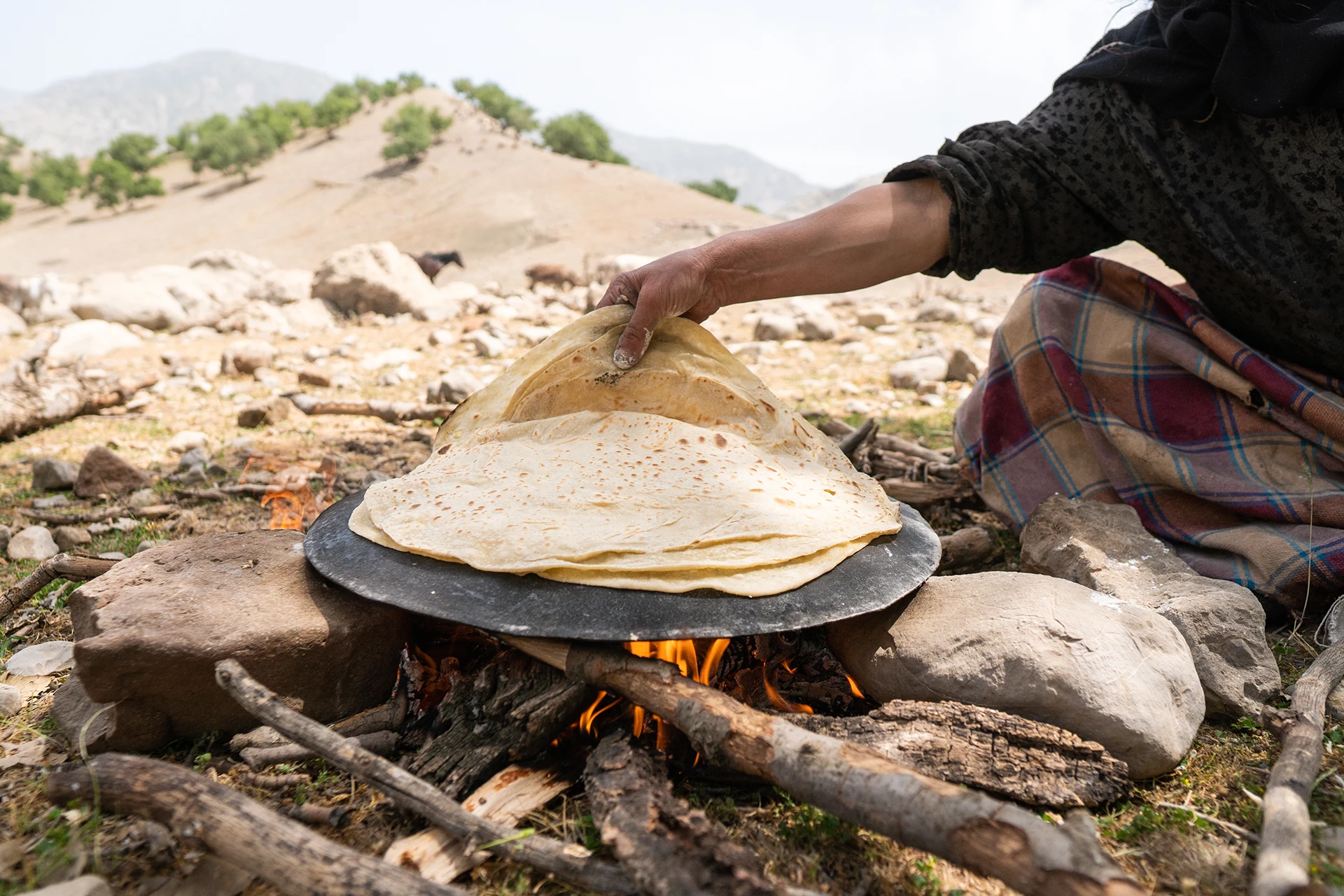 Hand die platbrood bakt boven een vuurtje in een droog landschap